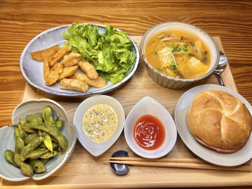 木のトレイに並べられた夜ごはんプレート。黒皮カジキのフライドポテト風、鶏団子のトマトスープ、枝豆、ソース2種、シズヤのカルネが美しく盛り付けられている。