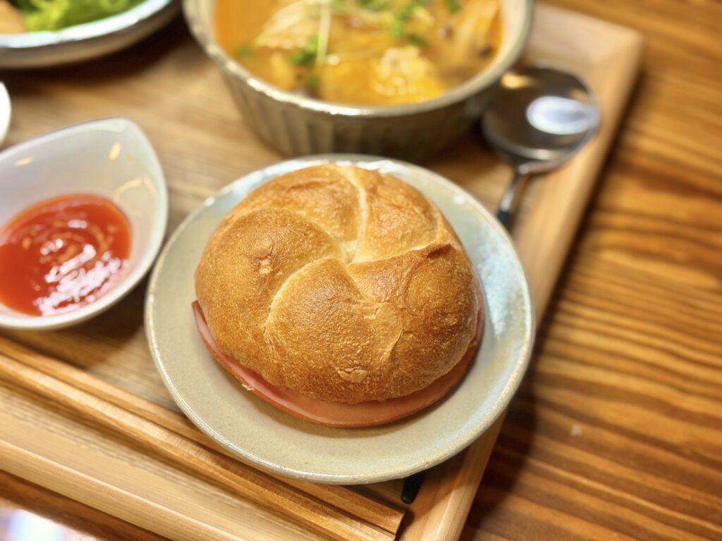 シズヤのカルネ。香ばしいフランスパンにハムを挟んだシンプルなサンドが、木のトレイの上で温かい光に包まれている。