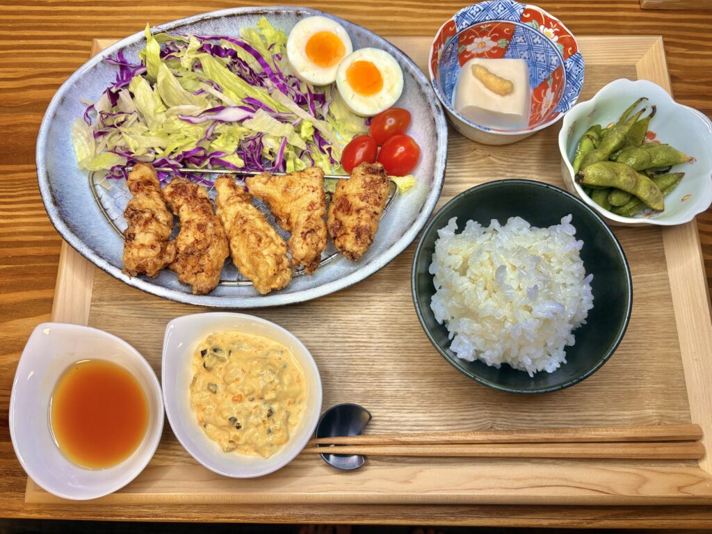 旦那キッチン特製のチキン南蛮定食。カリッと揚がったチキン南蛮に、シャキシャキ野菜のサラダ、半熟ゆで卵、枝豆、冷奴、白ごはん、タルタルソースと南蛮酢が添えられた家庭の食卓。