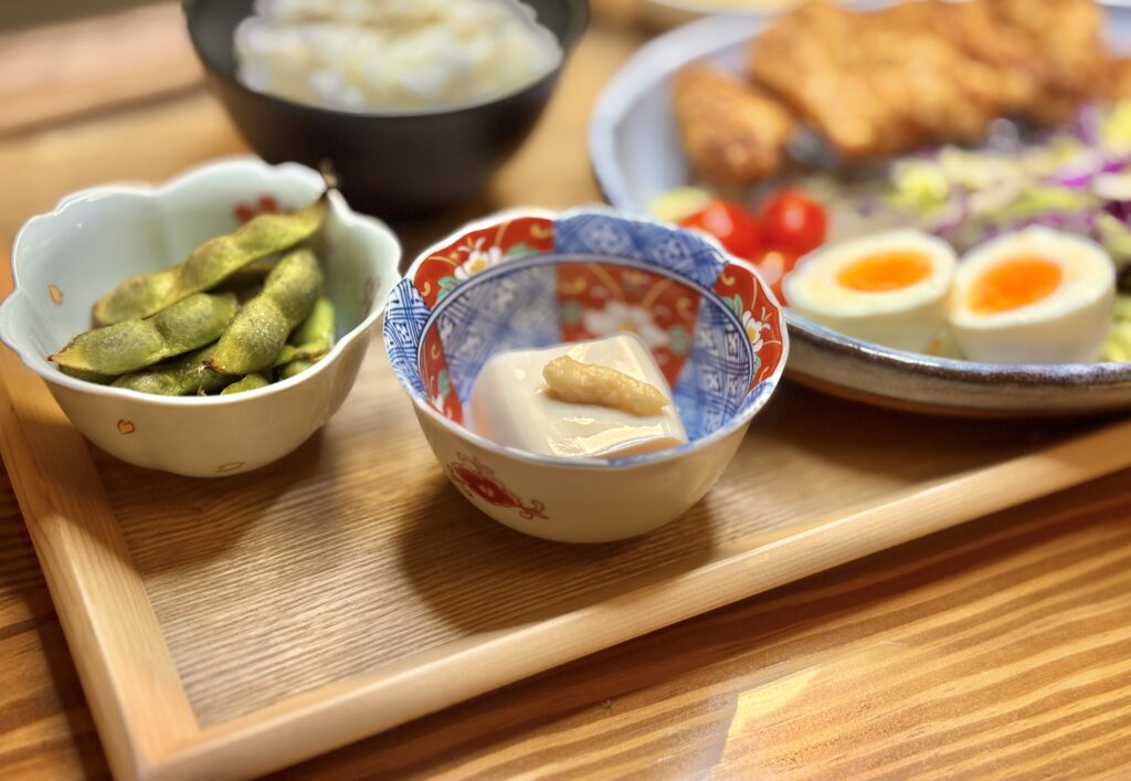 旦那キッチンの副菜。丹波篠山の黒枝豆と、しょうがを添えた冷奴。やさしい色合いの器に盛られた、家庭的で温かみのある一皿。」
