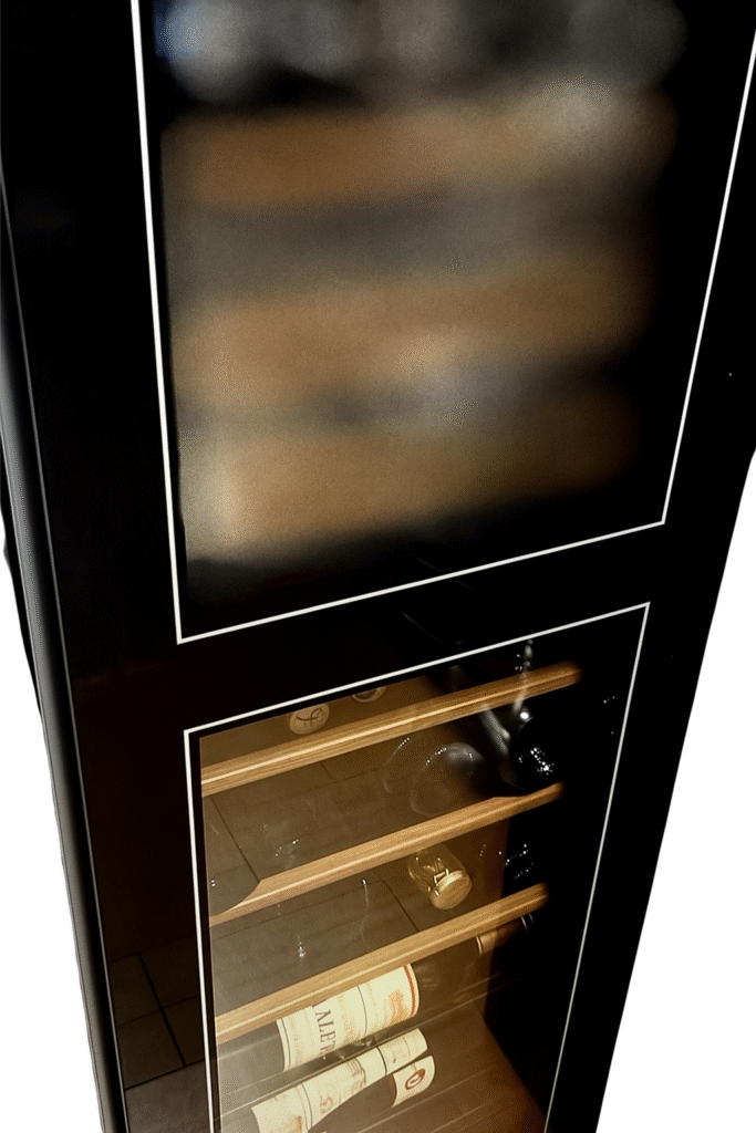 黒いガラス扉の大型ワインセラー。上段にはぼかしが入り、下段には数本のワインボトルが並んでいる。木製の棚が高級感を演出している。