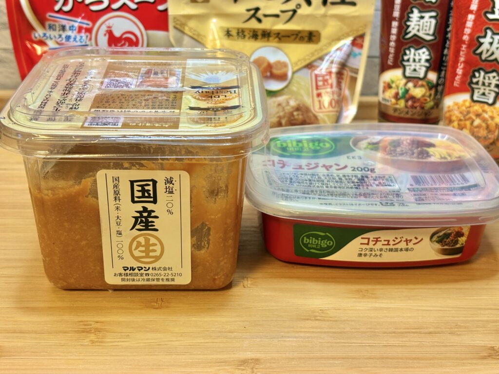 キムチ鍋の味付けに使う調味料を並べた写真。国産生みそ、bibigoのコチュジャン、丸鶏がらスープ、干し貝柱スープ、甜麺醤、豆板醤のパッケージがテーブルに置かれている」
