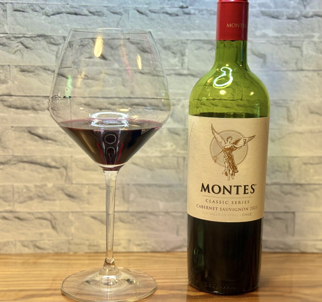 赤ワインが入った大きなワイングラスと、モンテスのカベルネ・ソーヴィニヨンのボトルが並べて置かれている写真。淡い石目調の背景の前で、深いルビー色のワインが映えている。
