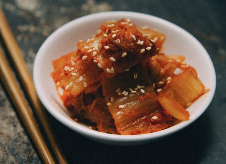 白い小皿に盛られた白菜キムチに白ごまを振りかけた一品。鮮やかな赤い色とごまの香ばしさが引き立つクローズアップ写真