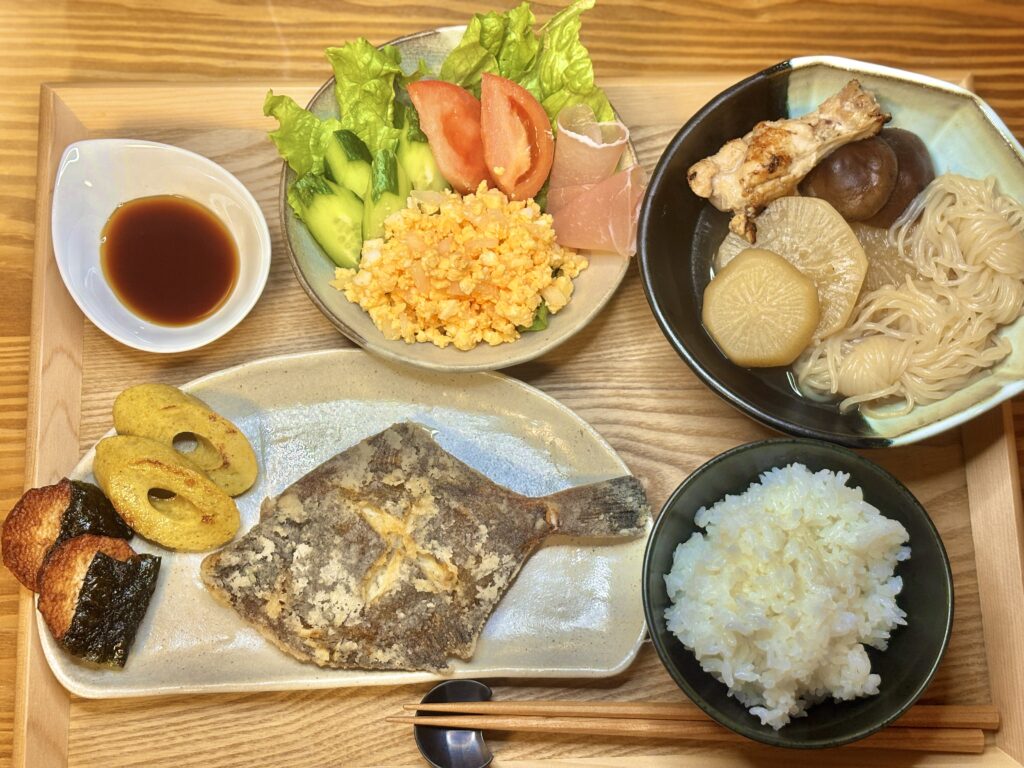 カレイの唐揚げと煮物、卵サラダ、生野菜、ごはんを並べた和食の晩ごはん
