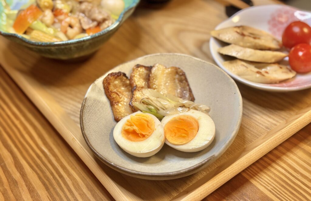 ネギチャーシューと半熟煮卵が白い皿に盛られ、隣に豆腐ちくわとミニトマトが並ぶ食卓の写真
