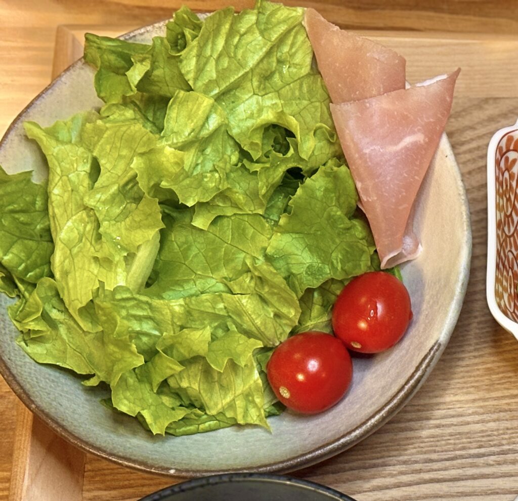 レタスにミニトマトと生ハムを添えたシンプルなサラダのアップ写真。