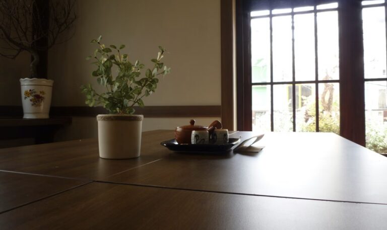 和室の窓辺に置かれた木製テーブルの上に、観葉植物と湯のみ、急須、小皿が並ぶ落ち着いた雰囲気の室内風景。