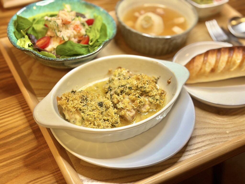 鳥もも肉の香草パン粉焼きを中心に、サラダやスープ、パンが添えられた食卓を横から写した写真。