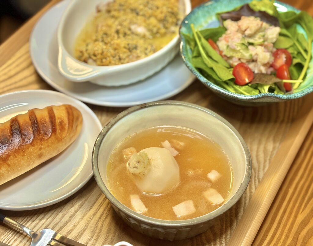 かぶを丸ごと煮込んだスープを手前に、パンと香草パン粉焼き、サラダが並ぶ食卓の様子。