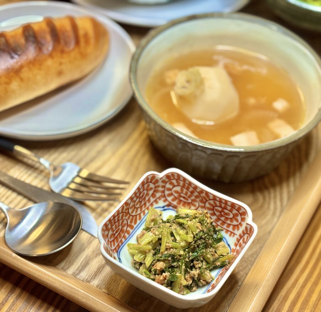 かぶの葉をおかかと胡麻で炒めた小鉢料理を、スープやパンと一緒に並べた食卓の一部。