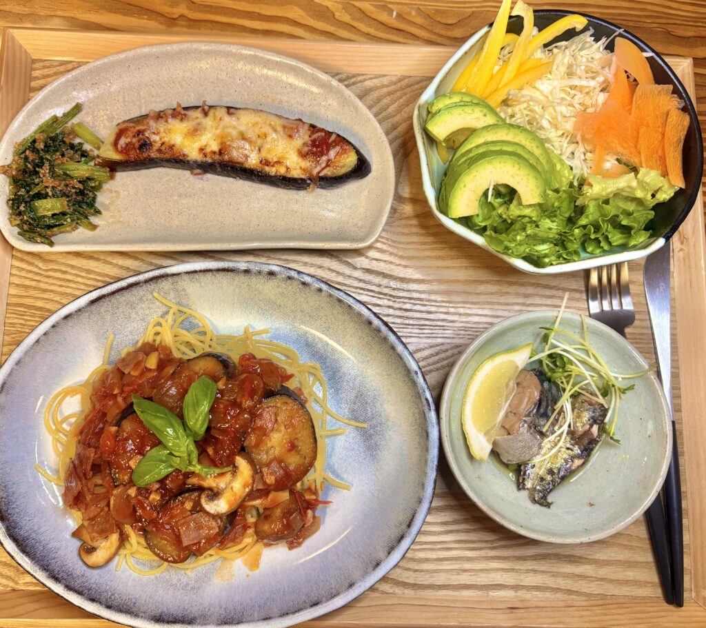 ・ナスのピザ風、ほうれん草のお浸し、具だくさんトマトパスタ、アボカドサラダ、いわしのレモン和えを並べた食卓の全体写真
