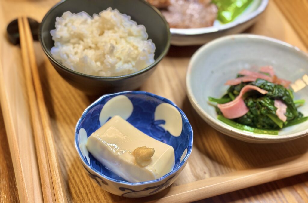 青い和柄の小鉢に盛られた冷奴。おろし生姜がのせられ、ご飯とほうれん草ベーコンの副菜が並ぶ和食の食卓シーン。