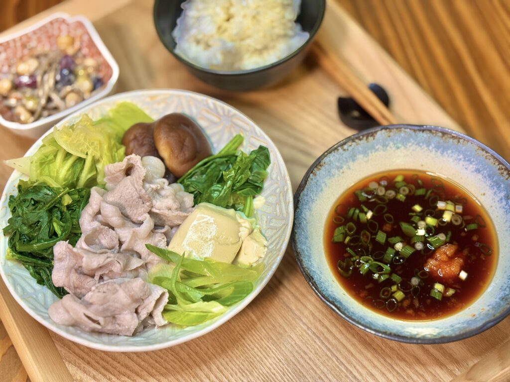 豚しゃぶと彩り野菜の盛り合わせ、ポン酢だれ、小鉢、ごはんを木のトレイに並べた和食献立の写真