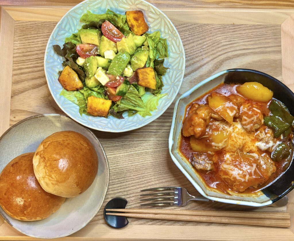 鶏肉のトマト煮とアボカドとかぼちゃサラダ、丸パンを並べた洋風献立のワンプレート写真