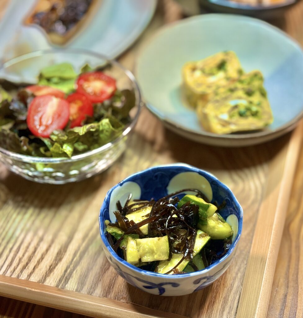 青と白の小鉢に盛られたきゅうりと細切り昆布の和え物。きゅうりの明るい緑と昆布の黒い艶が対比となり、木目のテーブルの上で瑞々しさが引き立つ一品