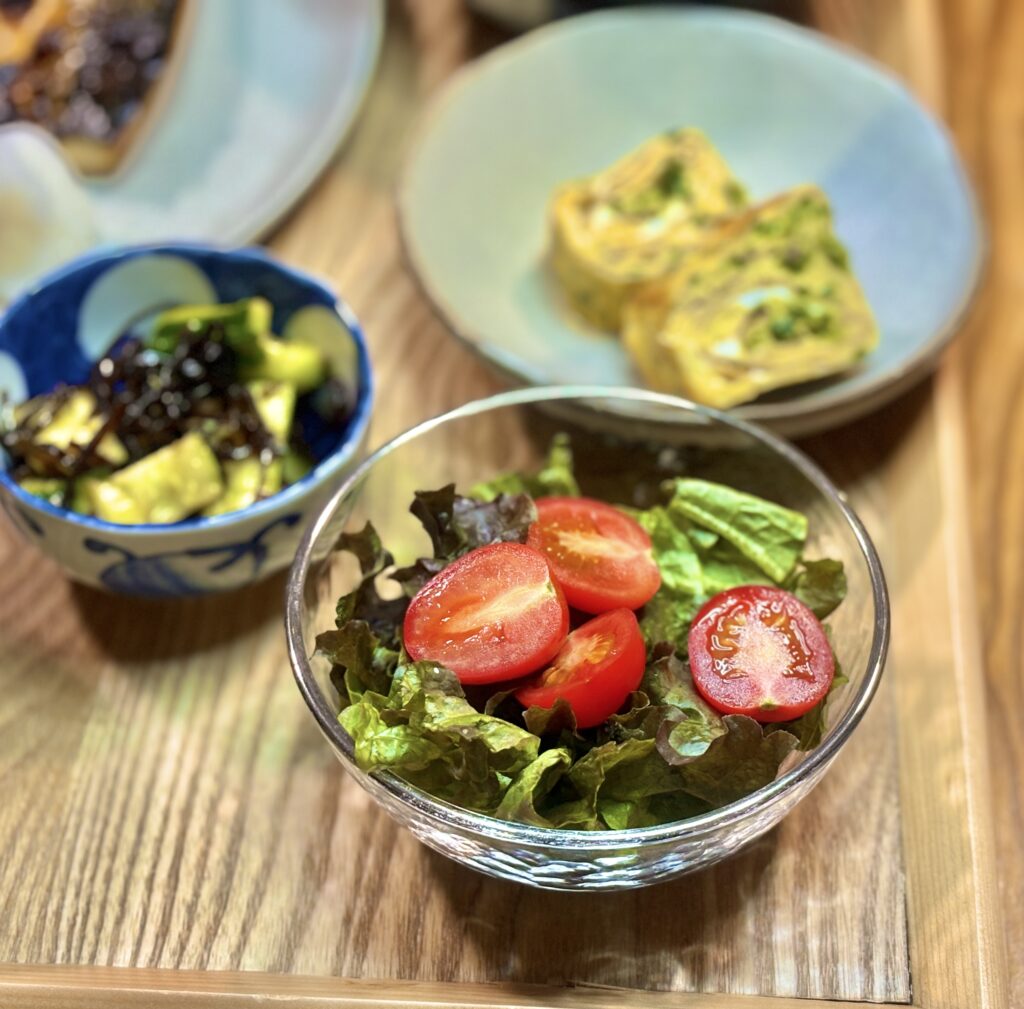 ガラスのボウルに盛られたサラダ。フリルレタスの上に、半分に切った赤いプチトマトが鮮やかにのっている。木目のテーブルの上で、瑞々しさが際立つ一皿