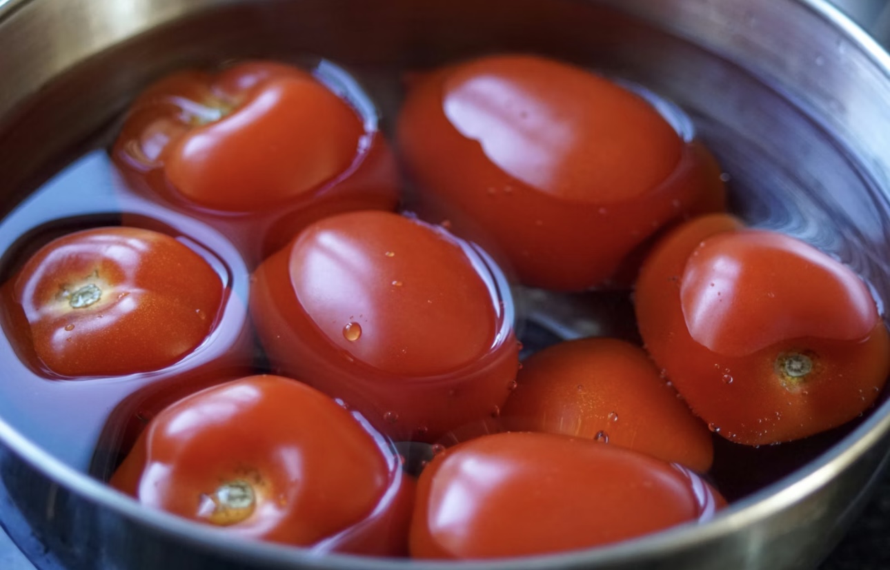 湯むき用に熱湯に浸したトマトが鍋に並んでいる写真。皮が取れやすい状態の真っ赤なトマトが浮かんでいる様子