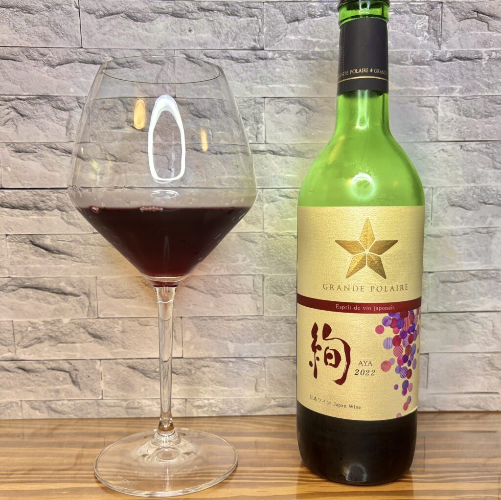 日本ワイン《絢 AYA》のボトルと赤ワイングラス。ベリーのような果実味が特徴の赤ワインの写真
