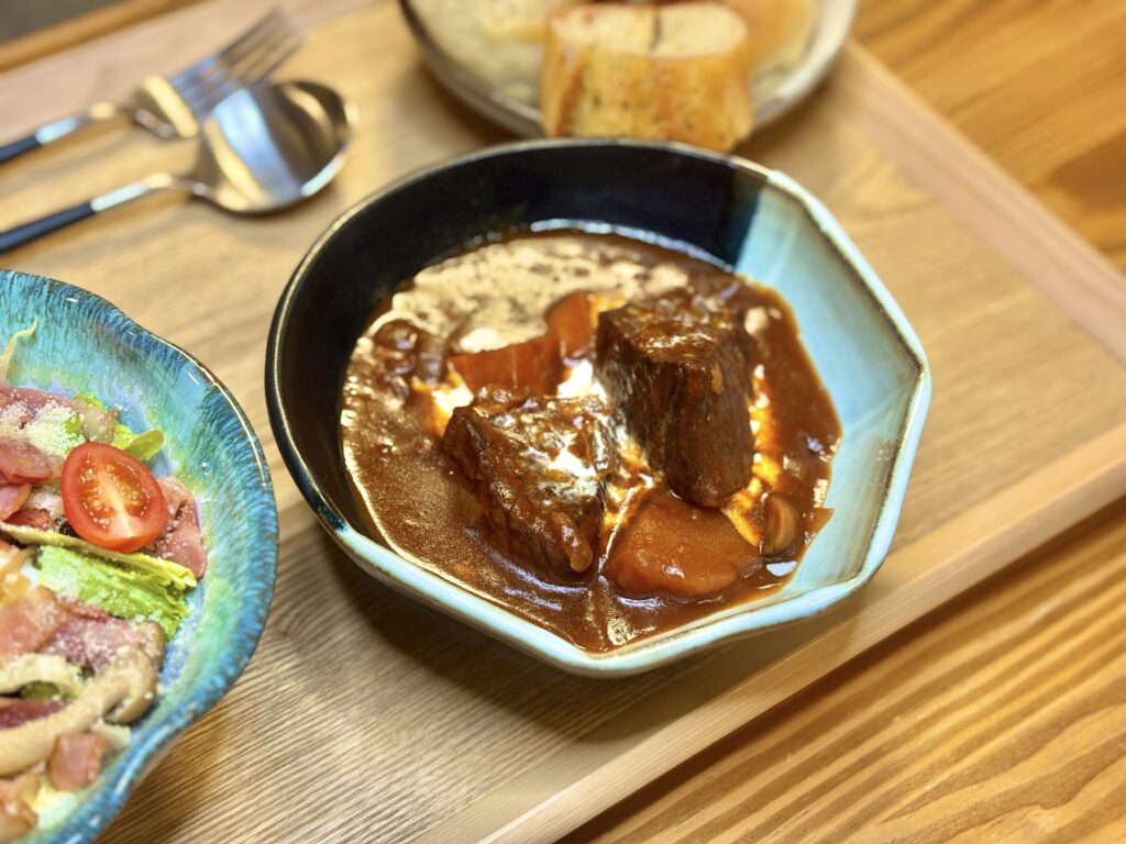 「ごろっと大きな牛肉が煮込まれたビーフシチュー。濃厚なデミグラスソースに野菜がとろけ、シーザーサラダとパンを添えたおうちレストラン風のディナー」