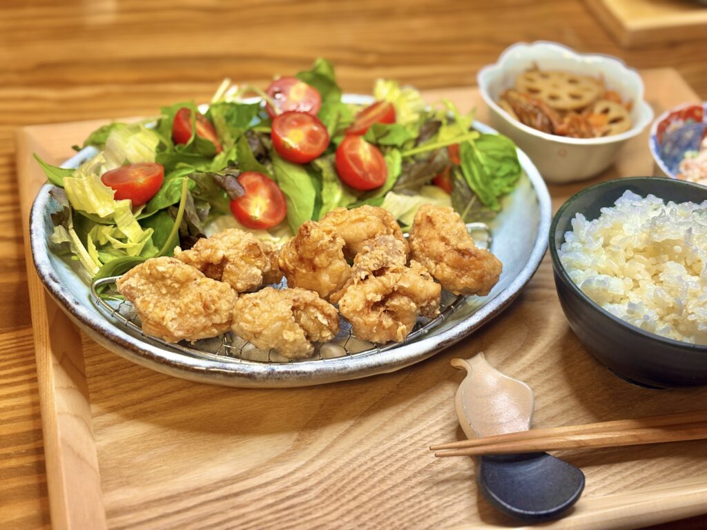 サクッと揚がった唐揚げとフレッシュなサラダ、白ごはんを盛り付けた夕食プレート。木のトレイの上に彩りよく並び、家庭的で温かみのある和食の食卓。