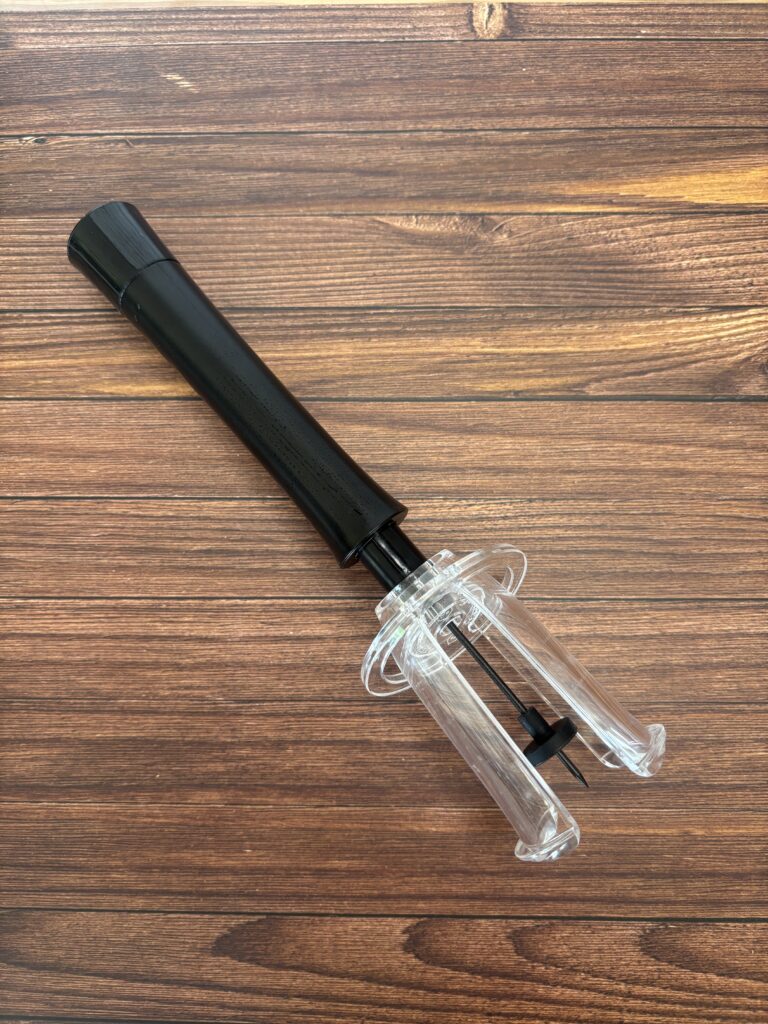 木目のテーブルの上に置かれた空気圧式ワインオープナー。黒い持ち手と透明なボディのシンプルでスタイリッシュなデザイン。