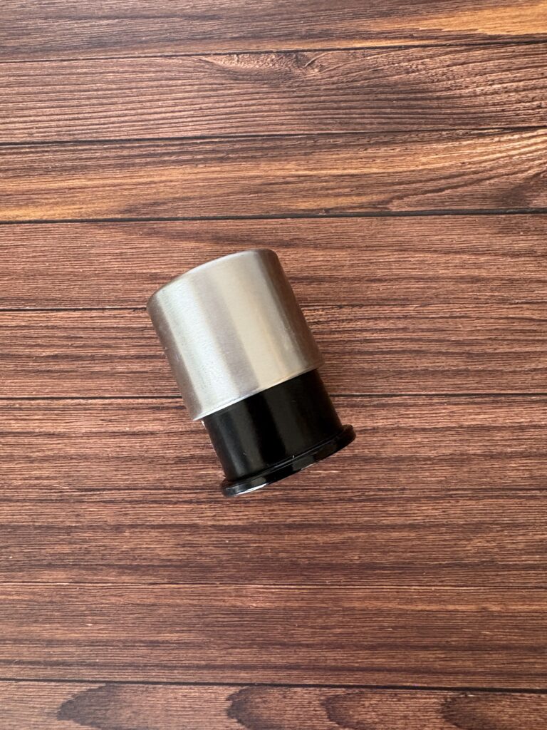 木目のテーブルの上に置かれたステンレスと黒のワインストッパー。真空タイプでシンプルかつモダンなデザイン。