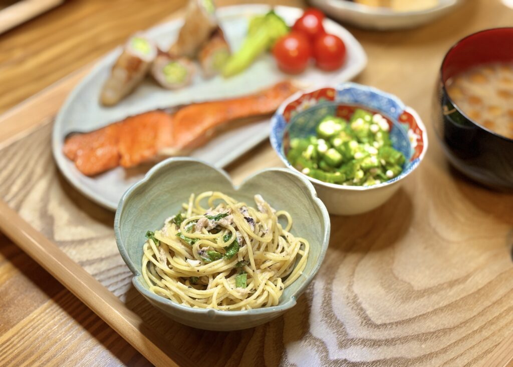 しらすと大葉のスパゲティを盛りつけた器を手前に、奥には塩しゃけ、オクラの豚肉巻き、オクラのおひたし、ミニトマト、なめこの味噌汁が並ぶ和洋ミックスの晩ごはん