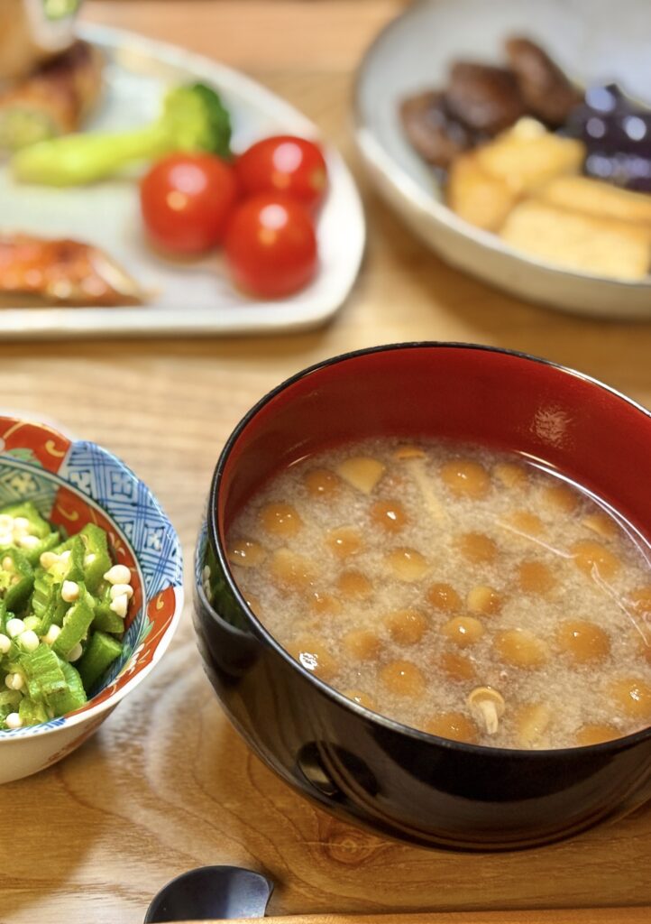 なめこの味噌汁を盛りつけた椀を手前に、奥にはオクラのおひたし、塩しゃけ、オクラの豚肉巻き、ミニトマト、茄子と椎茸の揚げ浸しが並ぶ温かみのある和食の食卓