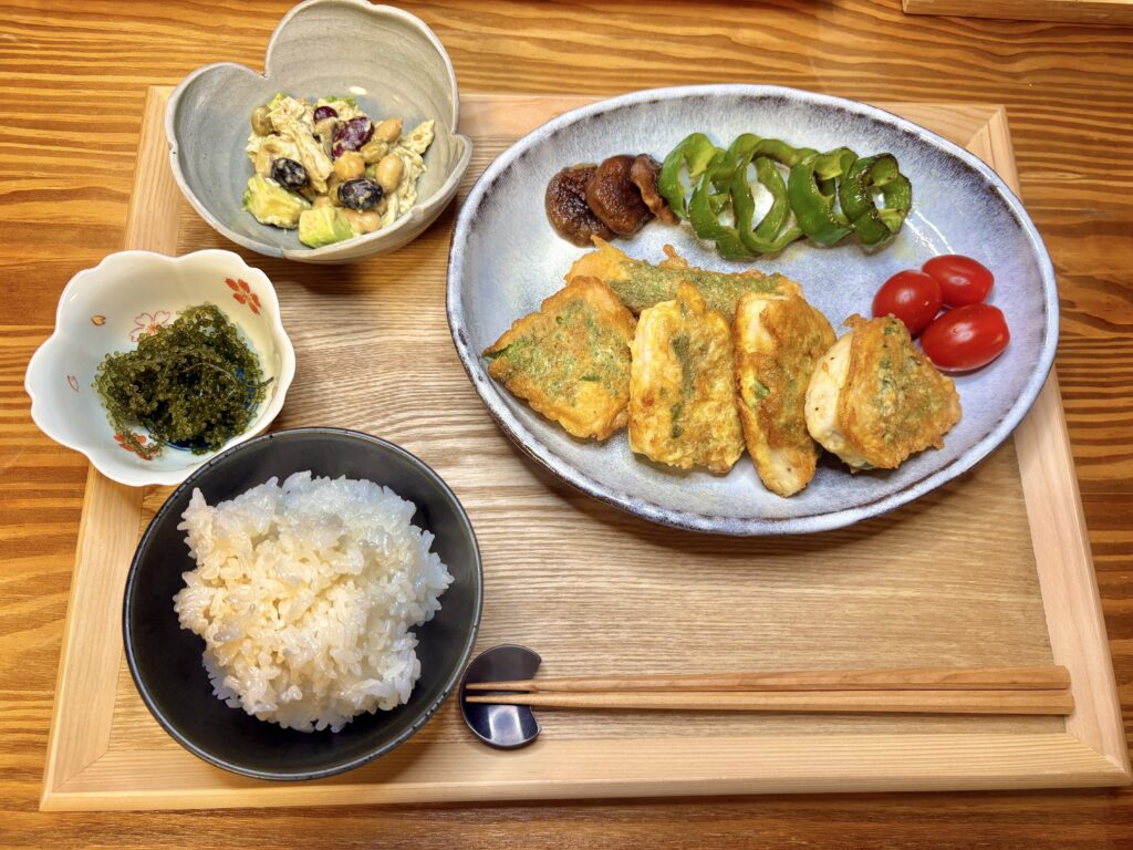 木のトレーに盛り付けた家庭の和食ごはん。黒皮カジキの青じそピカタ、焼きピーマンと椎茸、ミニトマト、副菜のアボカドと豆と鶏むね肉の胡麻あえ、海ぶどう、ごはんが並ぶ「旦那キッチン」の食卓。