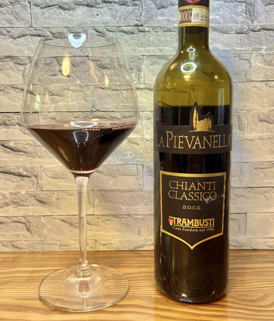 イタリア産赤ワイン『ラ・ピエヴァネッラ キャンティ・クラシコ』のボトルとワイングラス。深いルビー色のワインが注がれた上品な雰囲気の一枚。