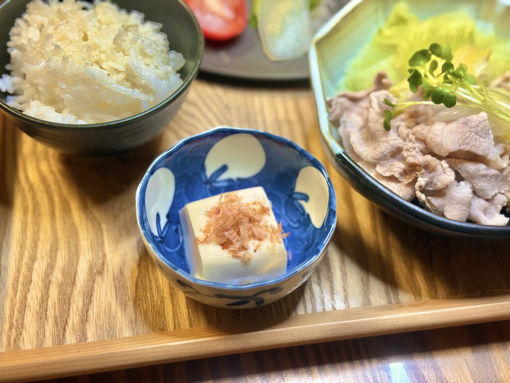 木のトレーに盛り付けられた冷奴とかつお節、炊きたての白ごはん、豚しゃぶ鉢が並ぶ和食の夕食セット