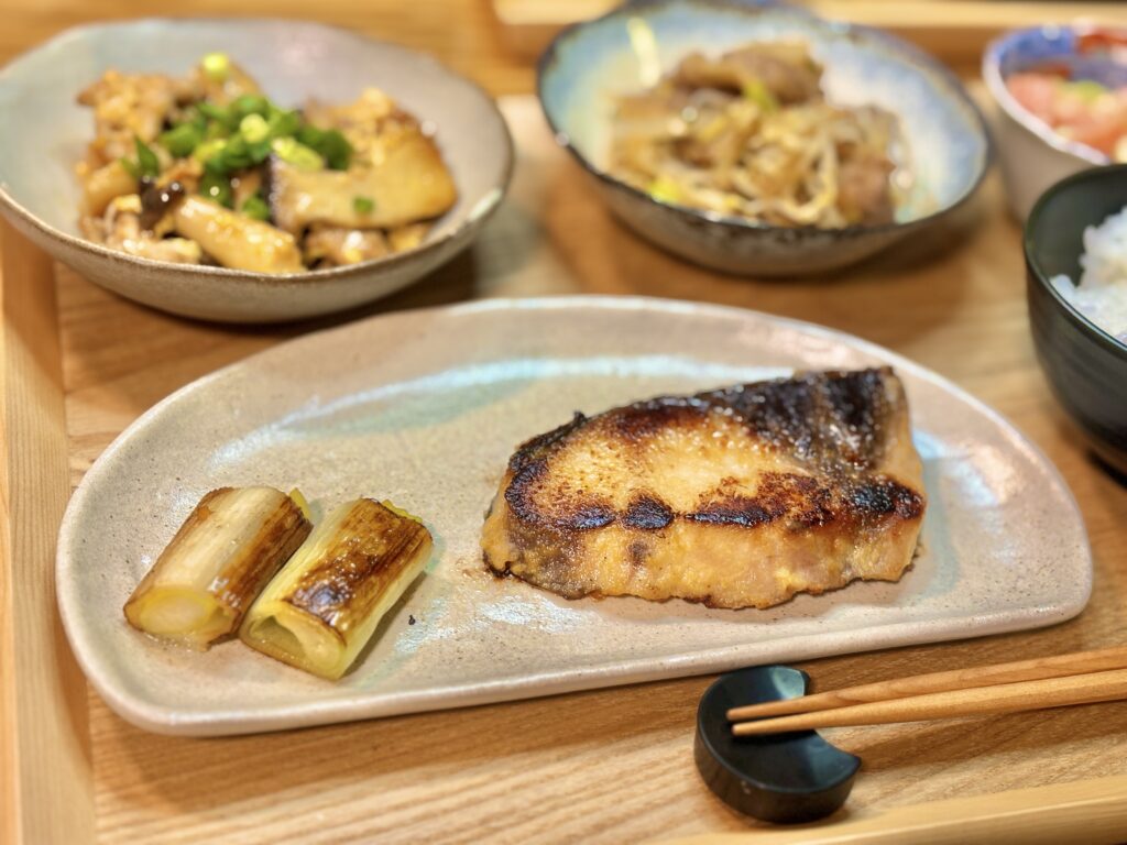 ぶりの味噌漬けと焼きねぎを盛りつけた和食メイン料理の写真。
