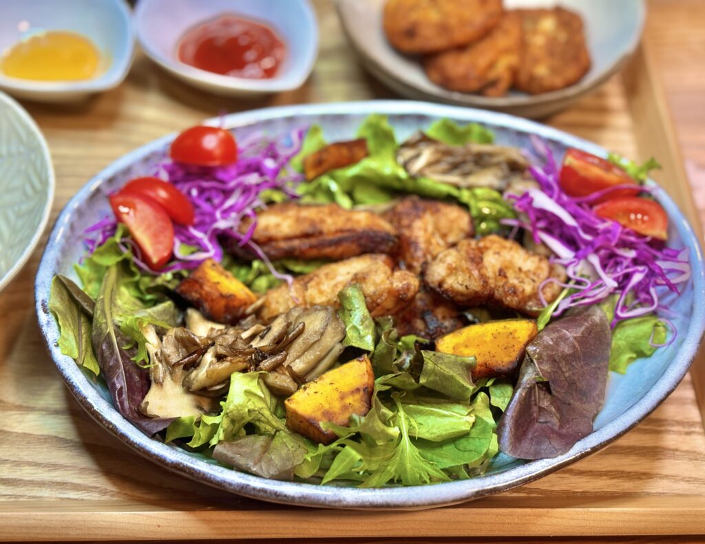グリルチキンと焼きかぼちゃ、舞茸、紫キャベツ、ミニトマトをのせた彩り豊かなサラダの写真。