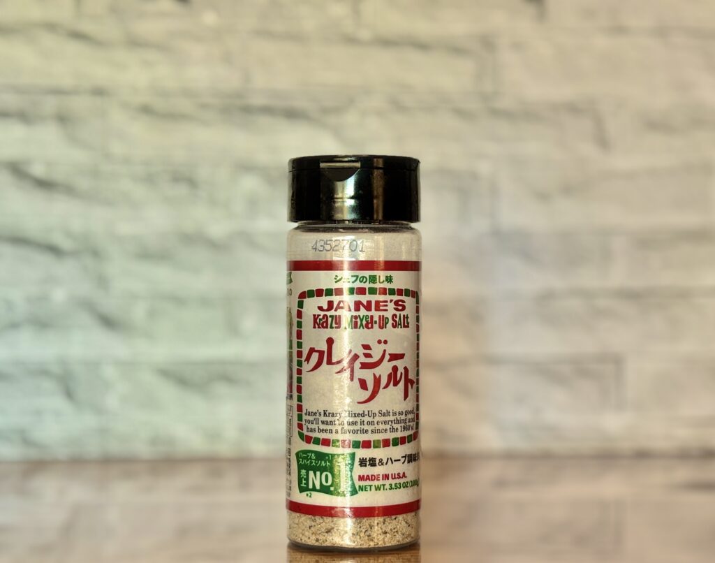 クレイジーソルトのボトルがテーブルの上に置かれ、背景のレンガ調とともに写されている写真。