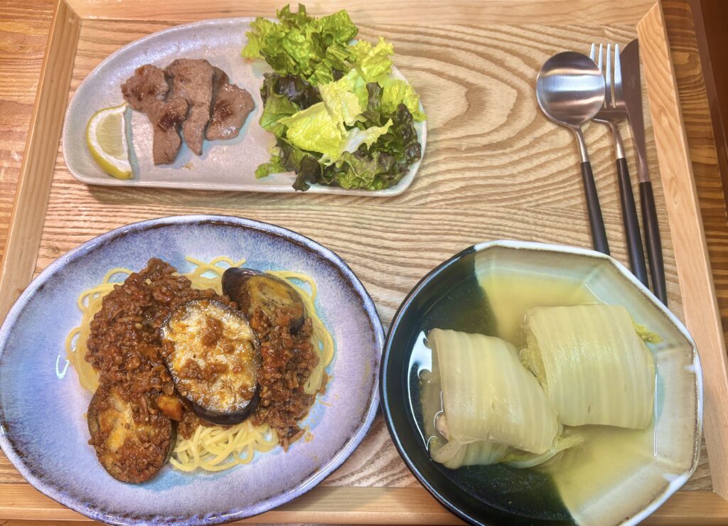 パスタ、ロール白菜、牛タン焼き、カトラリーが並べられた木製のトレー
