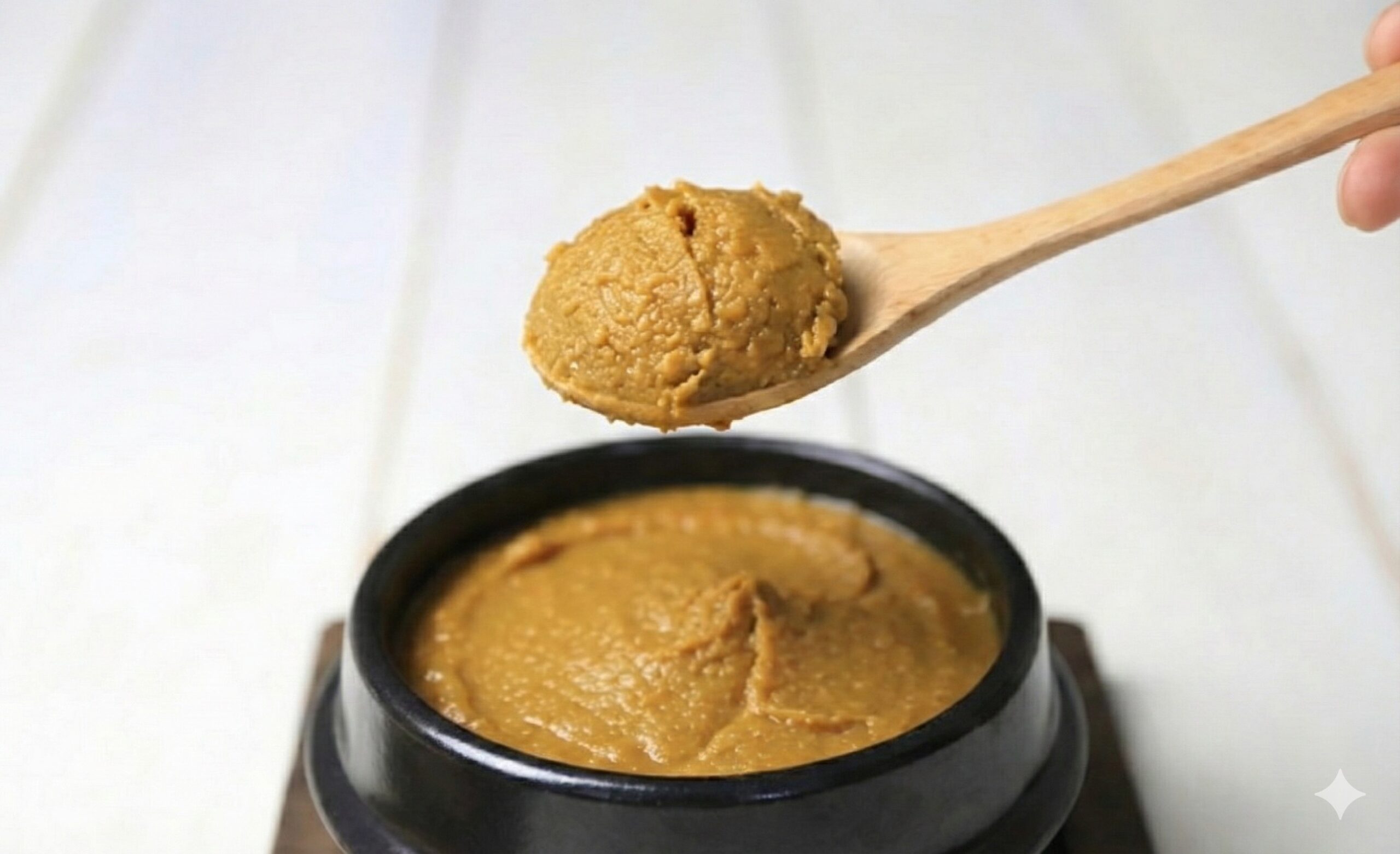 木のスプーンで味噌をすくい、黒い器に盛られた味噌の上に掲げた写真。