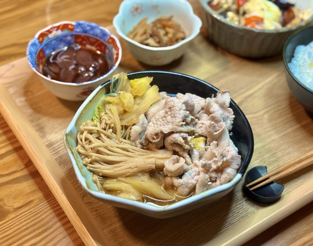 メイン料理の「豚肉と野菜の出汁しゃぶ」をアップで捉えた写真です。器には、ふっくらとした豚肉と、たっぷりのえのき茸、味が染みた白菜が盛り付けられ、出汁の優しい香りが漂ってきそうなシズル感があります。お肉と野菜の素材感が際立ち、ヘルシーながらも満足感のある一皿であることを強調しています。
