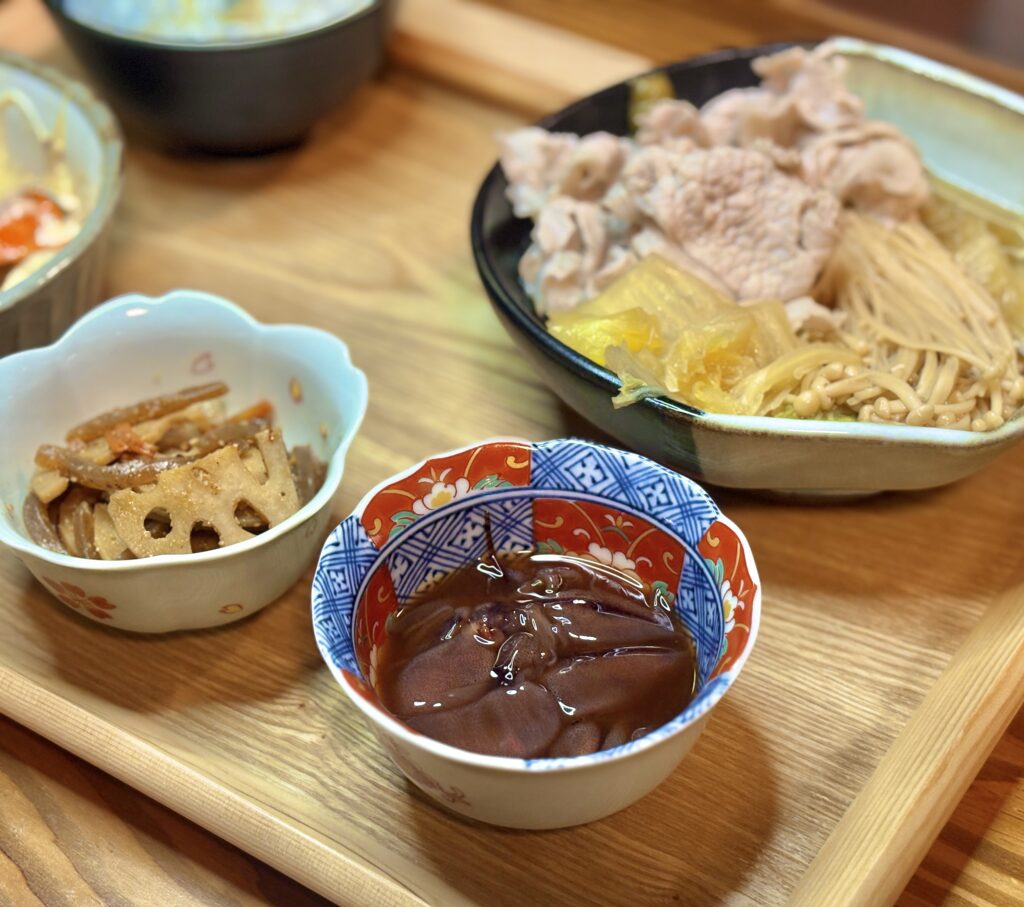 色鮮やかな和柄の小鉢に盛り付けられた、ホタルイカの醤油漬けのクローズアップ写真です。つやつやとした醤油ダレが絡んだホタルイカは、ご飯のお供やお酒の肴にぴったりの「名脇役」として、食卓に彩りとアクセントを添えています。
