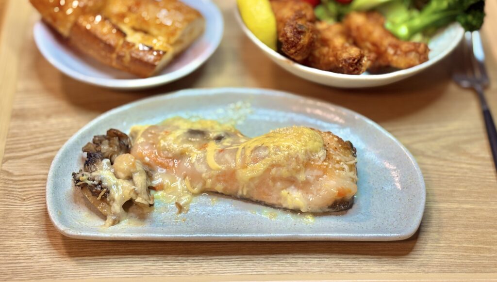 とろけたホワイトソースとチーズがかかったサーモンのチーズ焼きが、舞茸と一緒に皿に盛られているアップ写真。