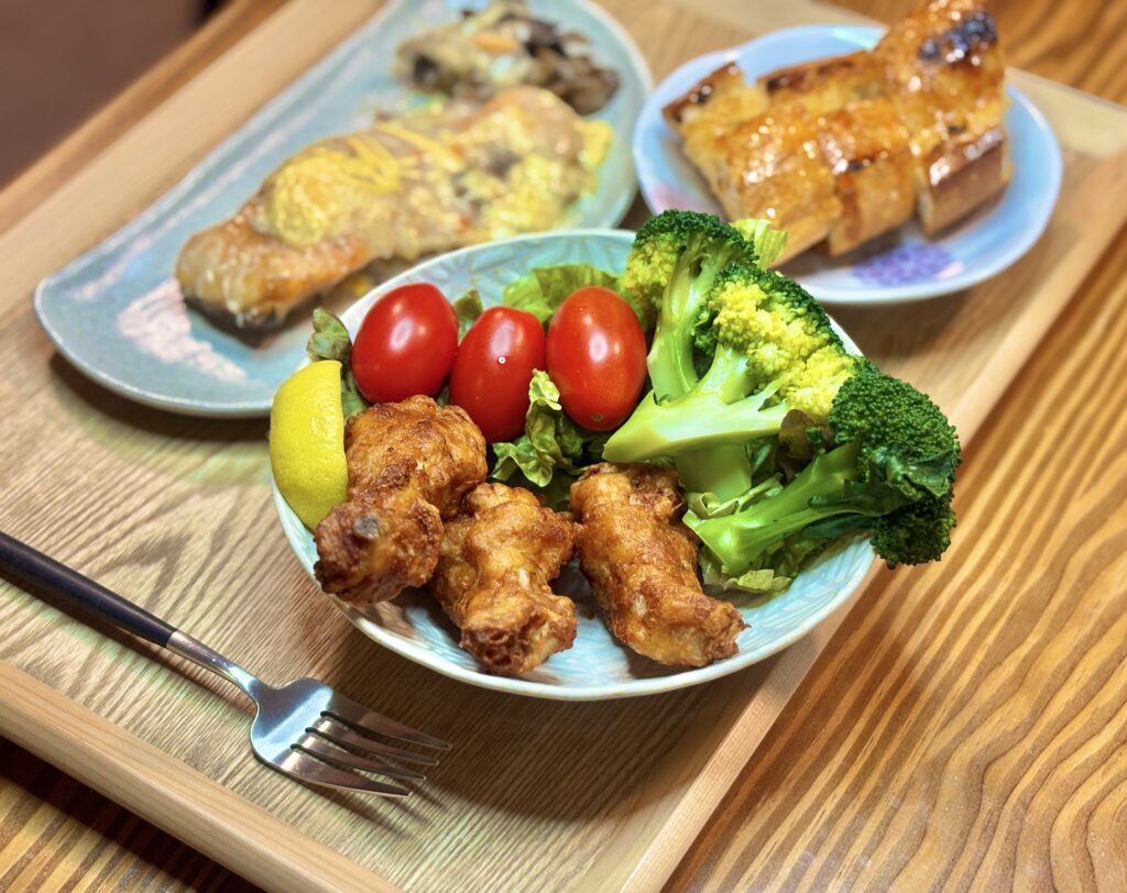 カリッと揚がったフライドチキンの横に、鮮やかなブロッコリーとミニトマト、レモンが添えられたサラダプレートのアップ。
