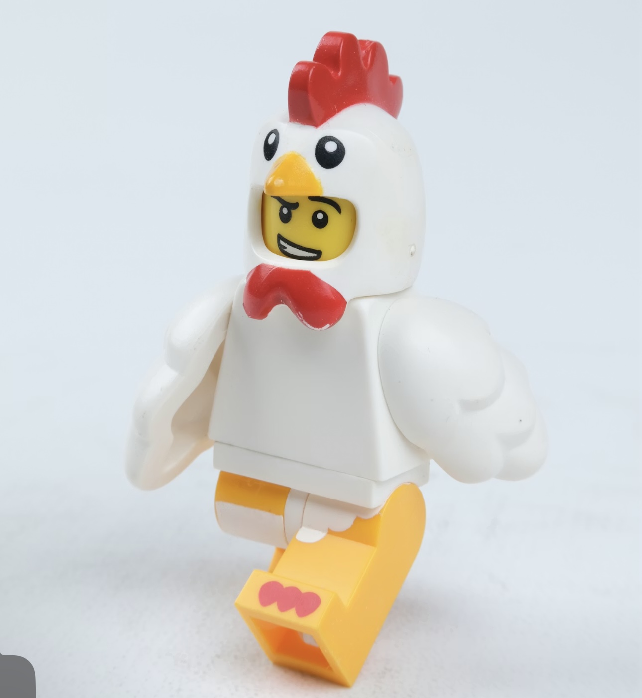 ニワトリの着ぐるみを着たレゴ風のキャラクターフィギュアが、軽く走り出すようなポーズをしている様子。