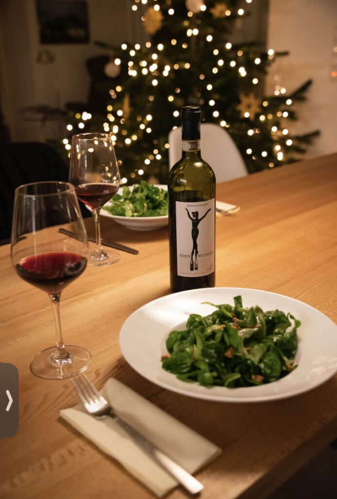 クリスマスツリーの明かりが灯る中、赤ワインとサラダが並ぶ温かい食卓の風景