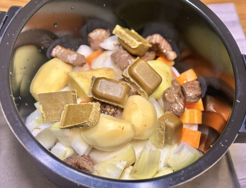 ホットクックの内鍋に入れたビーフカレーの具材の写真。カットされた牛肉、じゃがいも、玉ねぎ、人参の上に、固形のカレールーがそのまま乗せられている調理前の様子。