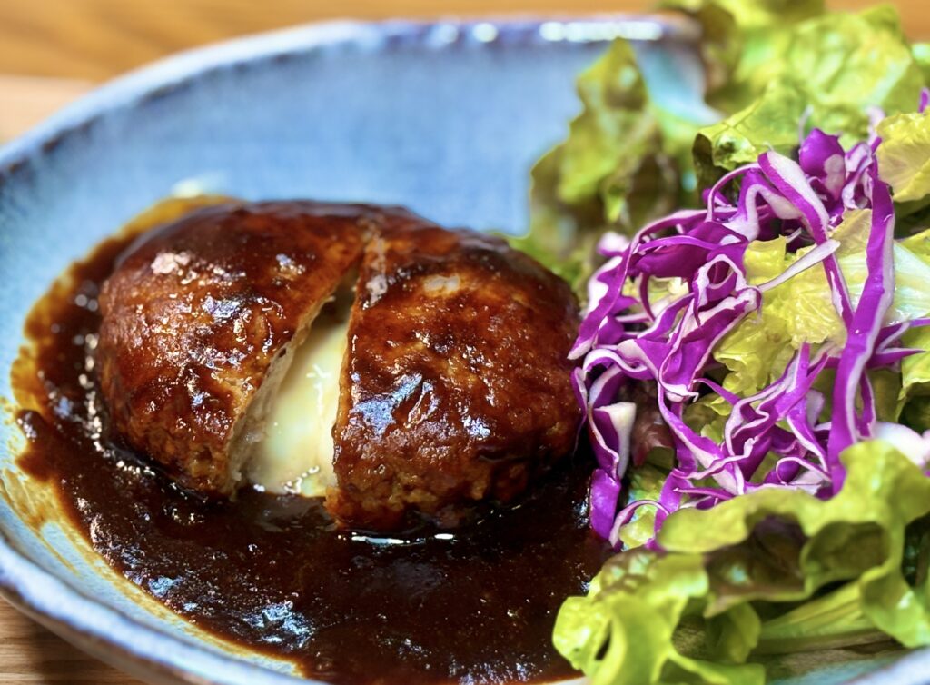 表面に照りのあるデミグラスソースをまとったチーズインハンバーグ。切り込みから中のチーズが溶け出し、食欲をそそる仕上がりになっている。