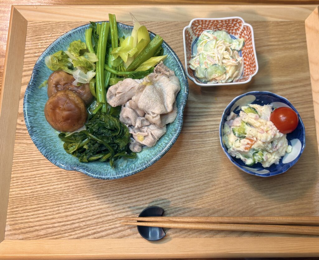 木のトレーの上に並べられた和食の献立、豚しゃぶと野菜の盛り合わせ、小鉢2品と箸が整えられている