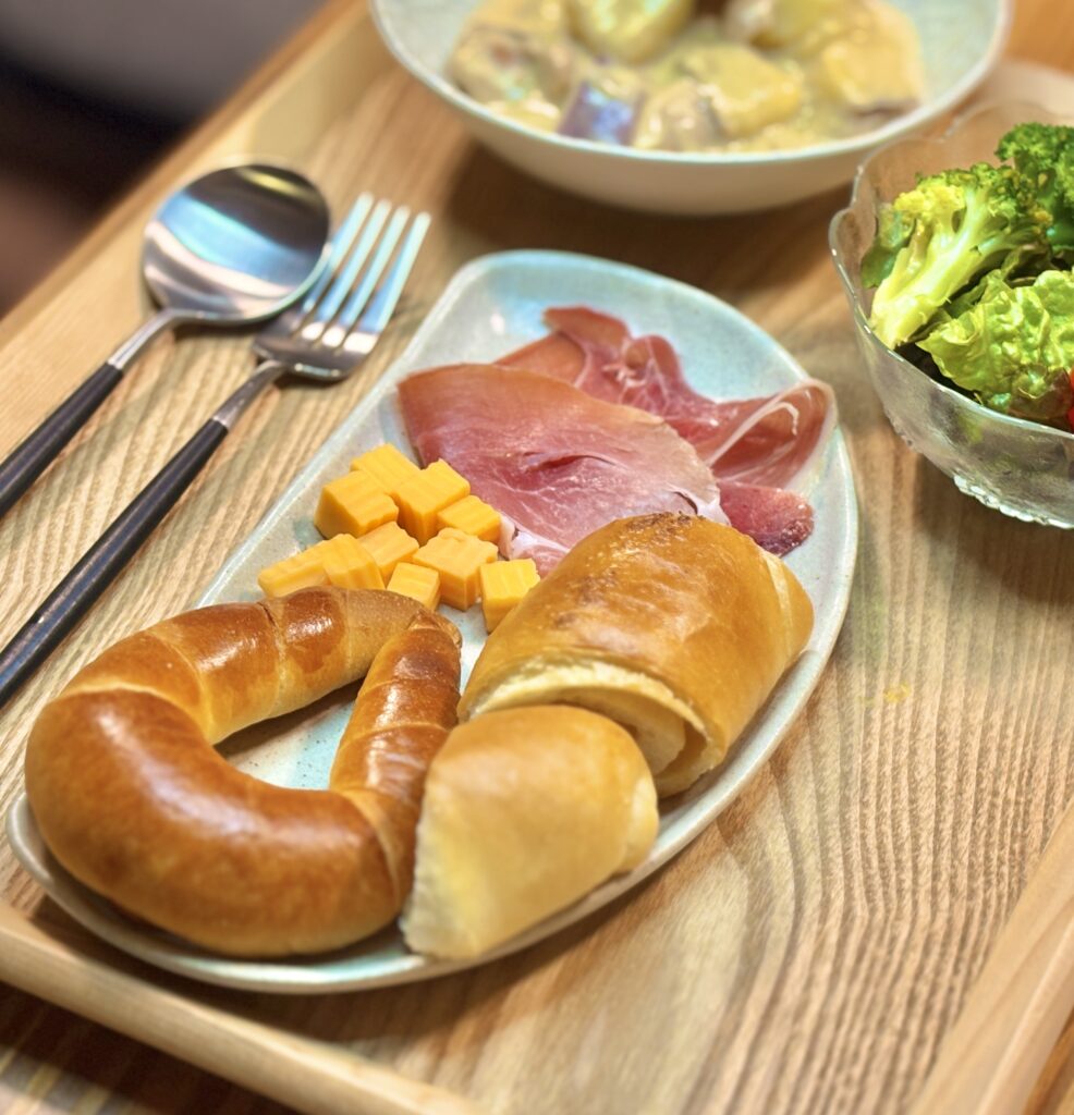 イスズベーカリーのパンと生ハム、角切りチーズをワンプレートに盛りつけた写真。横にはサラダとカトラリーが添えられている。