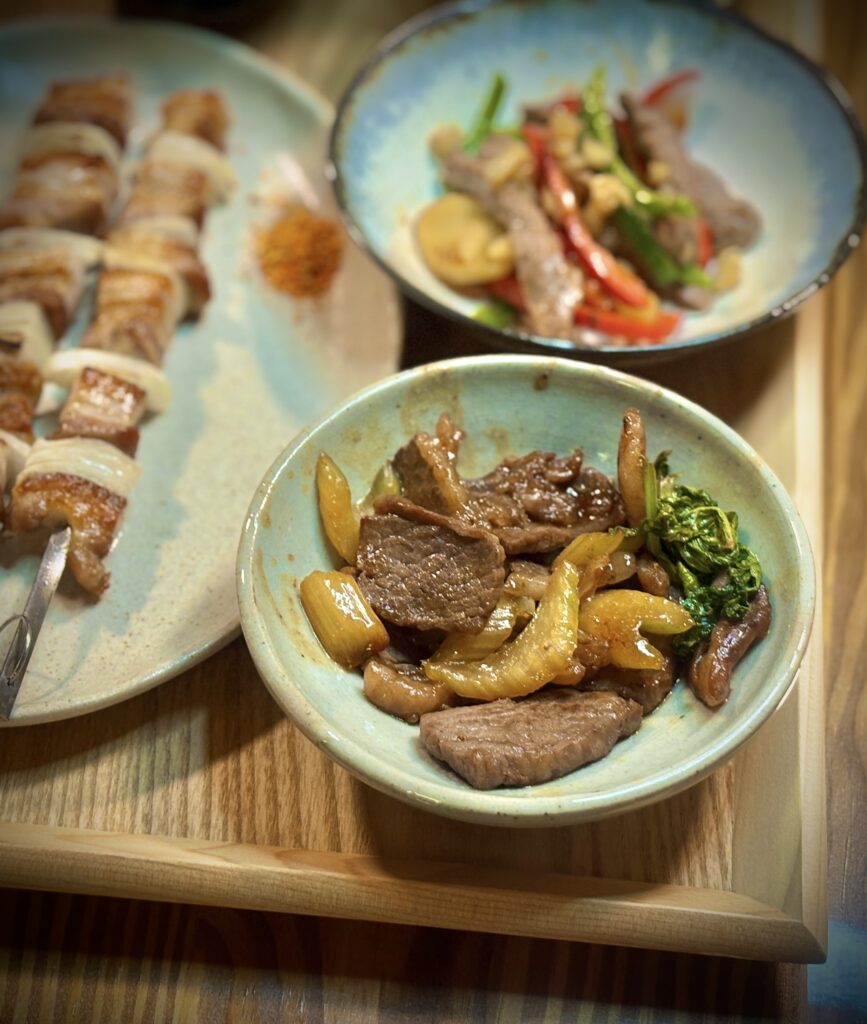 牛肉と玉ねぎ、青菜を甘辛く炒めた副菜を器に盛りつけた様子。照りのある仕上がりで食欲をそそる一品。