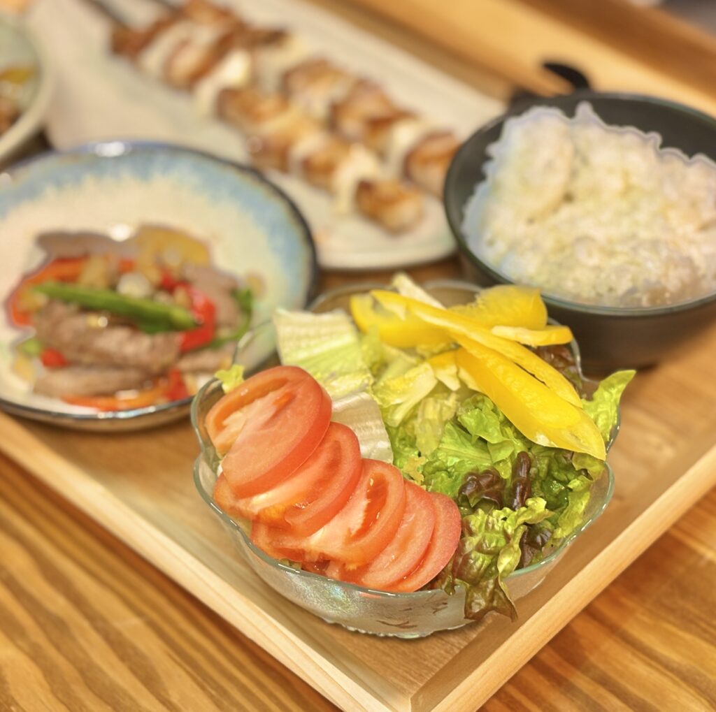 トマトとリーフレタス、黄色パプリカのサラダと、つやのある白ごはんを並べた食卓の一場面。