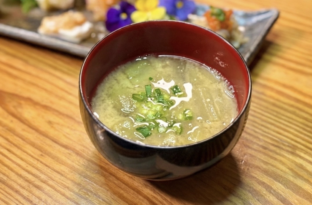 木目のテーブルの上に置かれたお椀に入った、刻み海苔が浮かぶ温かい青のりたっぷりの味噌汁。食卓の一品として並んだ家庭的な雰囲気が伝わる写真